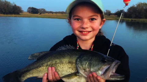 A child of a happy client holding a bass she caught in her family pond.